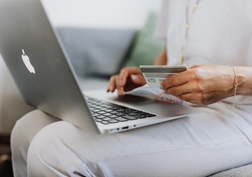 person using a macbook and holding a credit card